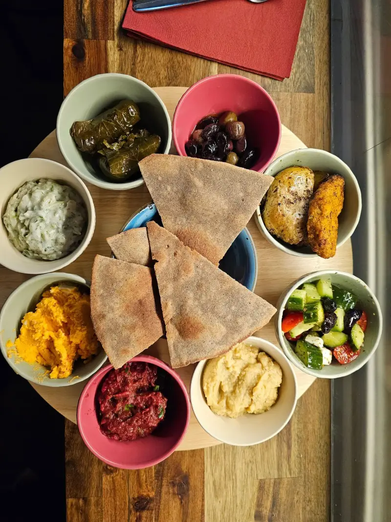 Mezze mit Dips, Dolmades, Oliven und Fladenbrot in bunten Schälchen